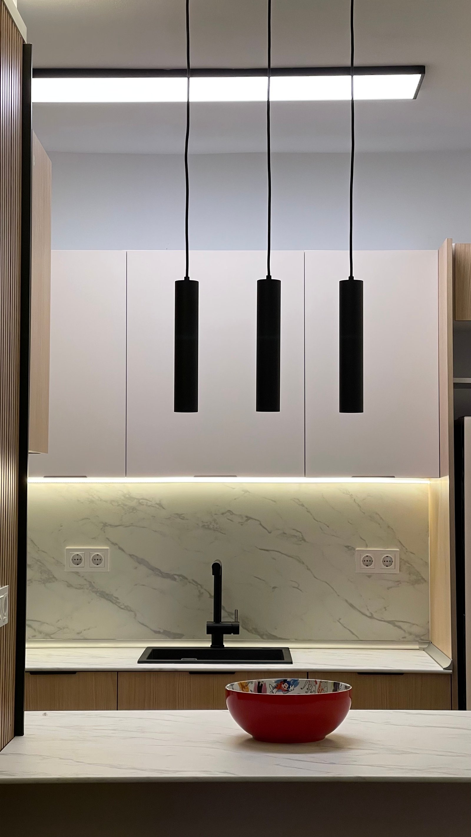 Muebles altos blancos y frontal de mármol con lámparas colgantes