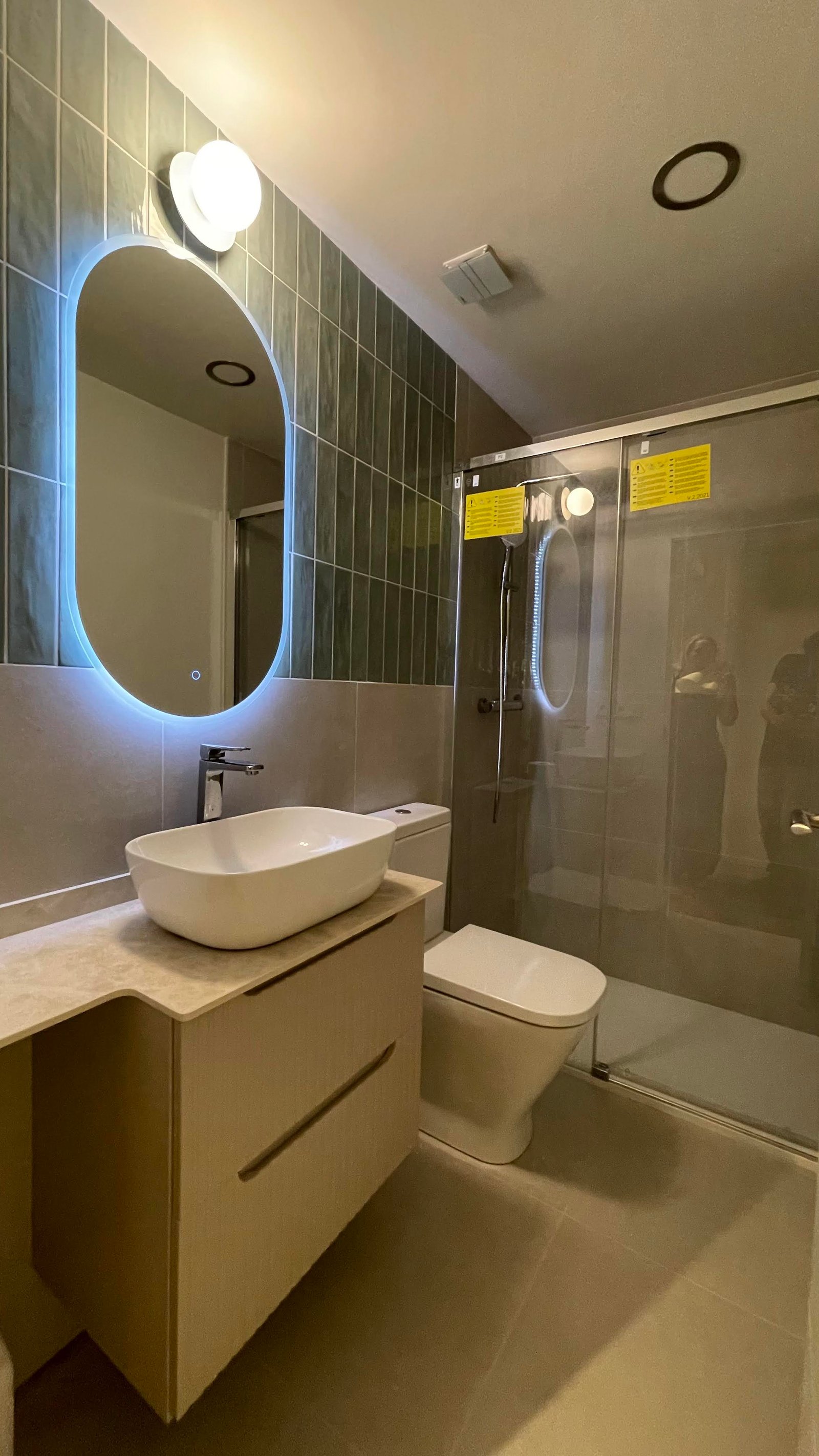 Baño terminado con espejo ovalado retroiluminado y ducha